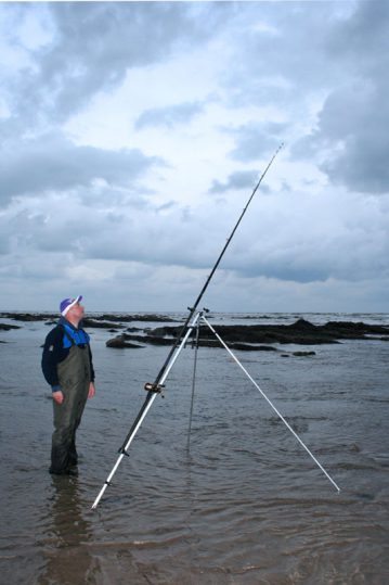 an angler on a rocky sore watches his rod tip